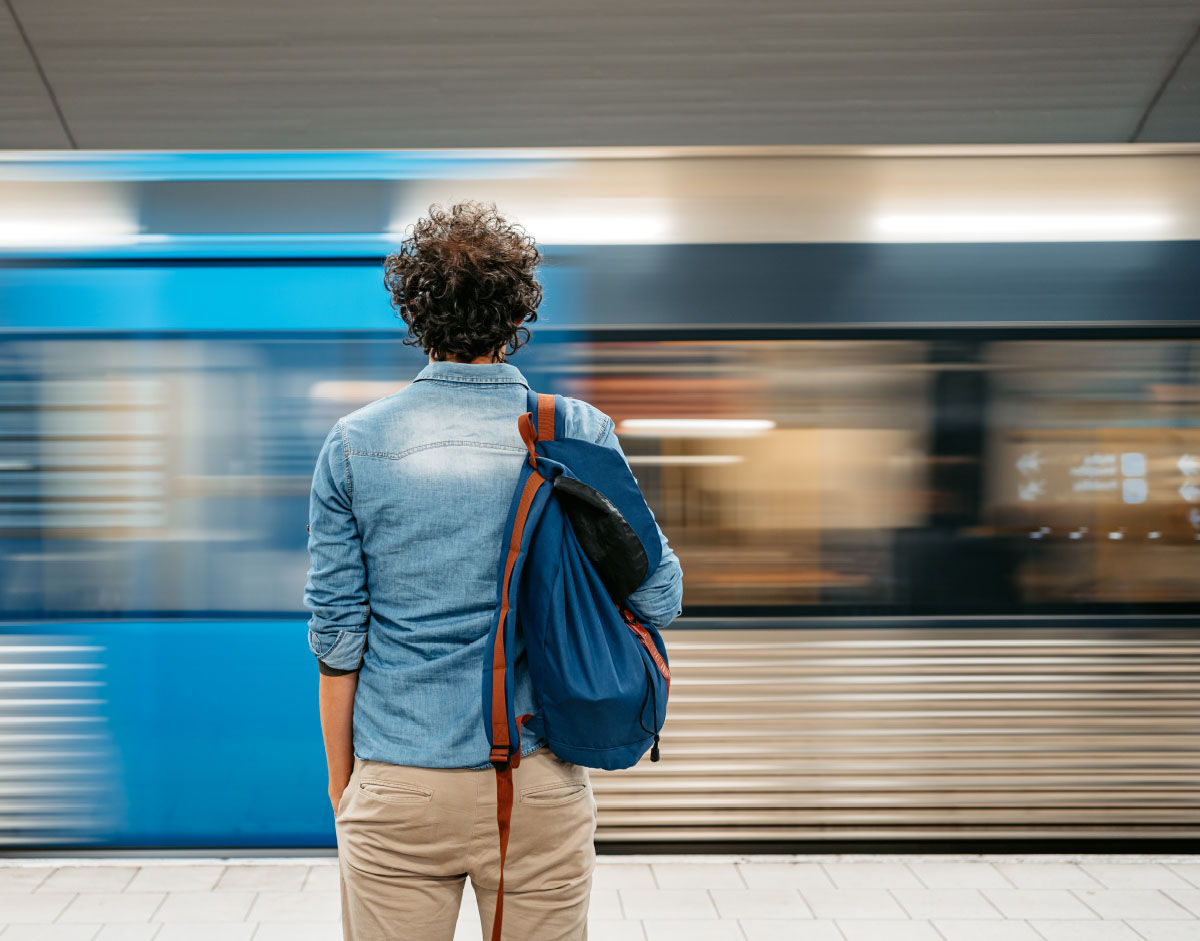 Man with backpack standing facing a movimg subway train